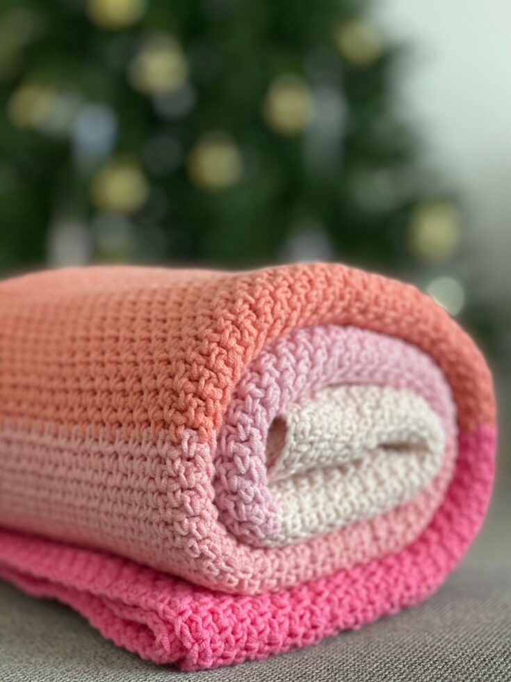 Soft colorful handmade crochet baby blanket rolled on a cream surface
