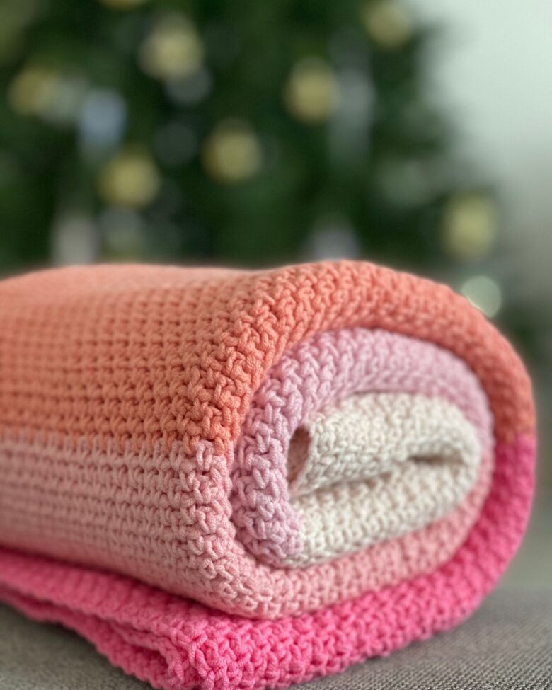 Soft colorful handmade crochet baby blanket rolled on a cream surface
