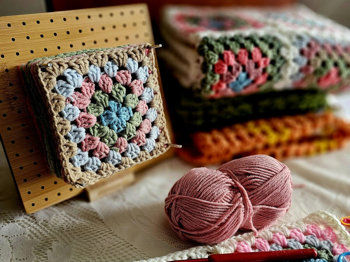 Pastel granny squares with yarn, a crochet hook, and scissors arranged on a soft cream bed