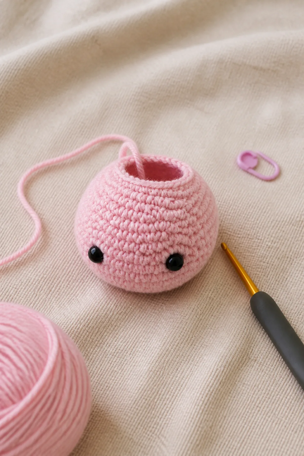 Rounded pink crochet axolotl head in progress with installed black safety eyes