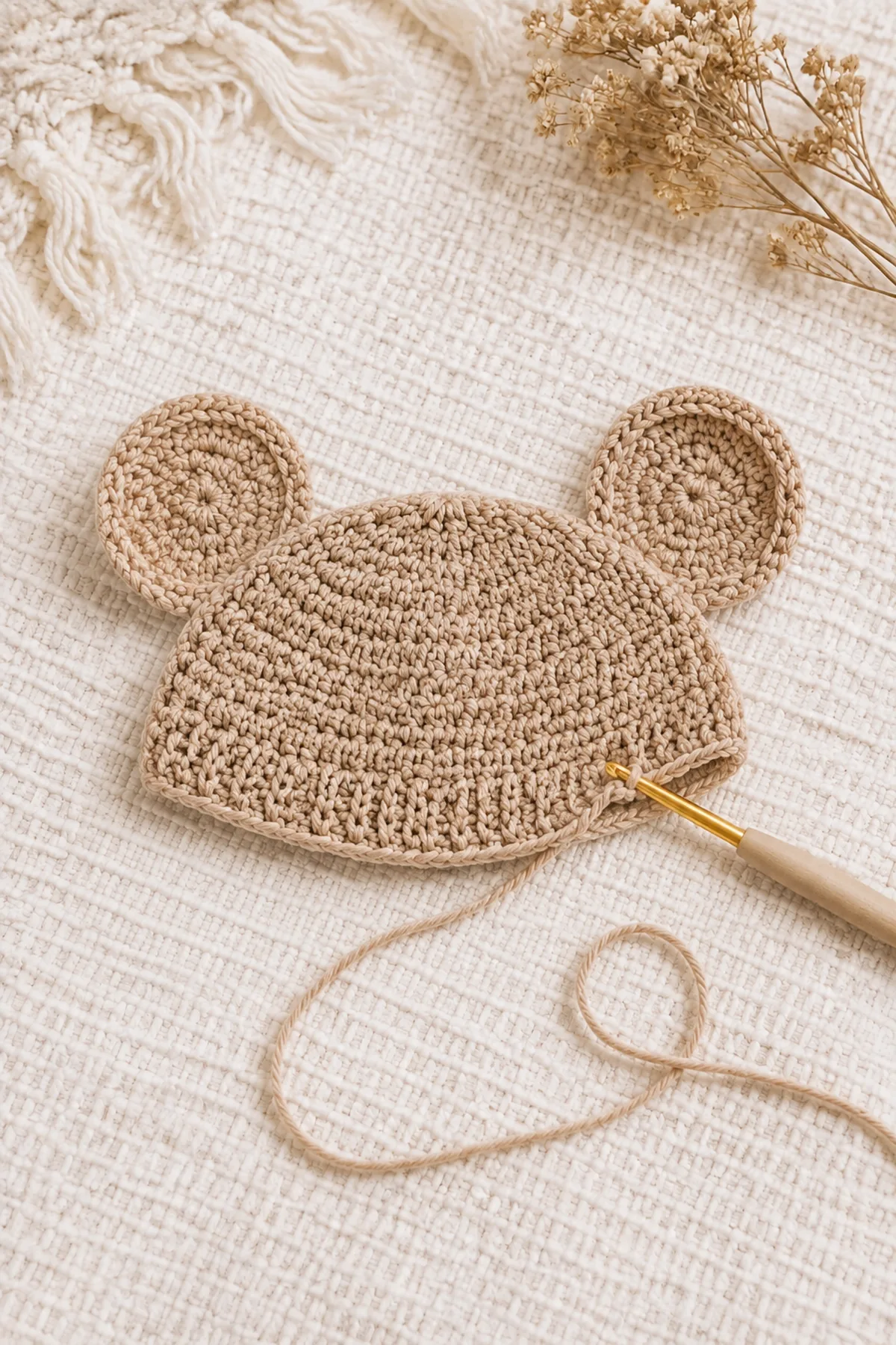 Early crochet construction stage for easy crochet bear ear baby hat with working yarn and hook